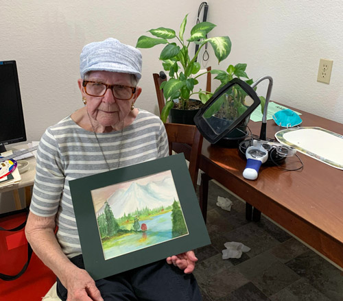 Pat holding a painting she did with her new magnifiers from the Older Individuals with Blindness Program at DAC